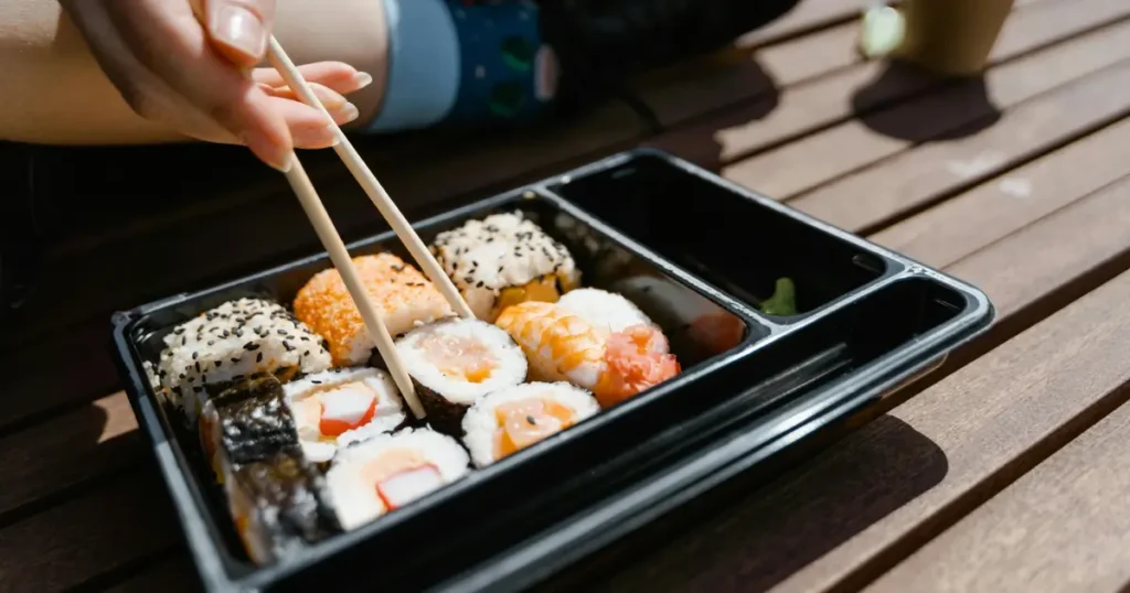 Close-up of a sushi salmon bake with layers of creamy, seasoned rice, topped with a golden-baked layer of salmon mixed with spicy mayo and melted cheese. Garnished with chopped green onions, sesame seeds, and a drizzle of soy sauce and sriracha, adding vibrant colors and textures