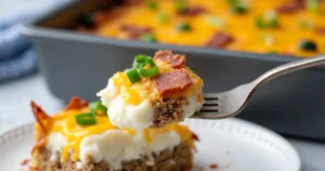 A rustic, cozy kitchen with a golden cowboy meatloaf and potato casserole on a wooden table, surrounded by ingredients like fresh herbs and potatoes.